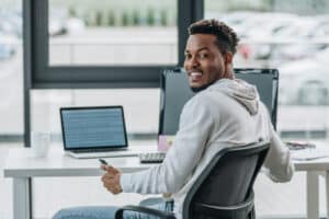 happy african american programmer smiling at camera while sitting at workplace in office