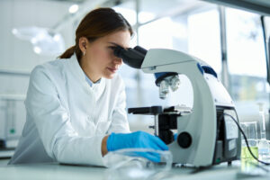 Young female scientist working on a research through a microscope in laboratory.