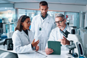 Discussion, science and tablet with people in laboratory together for breakthrough or development. Conversation, laptop and microscope with professional research team in clinical trial for discovery