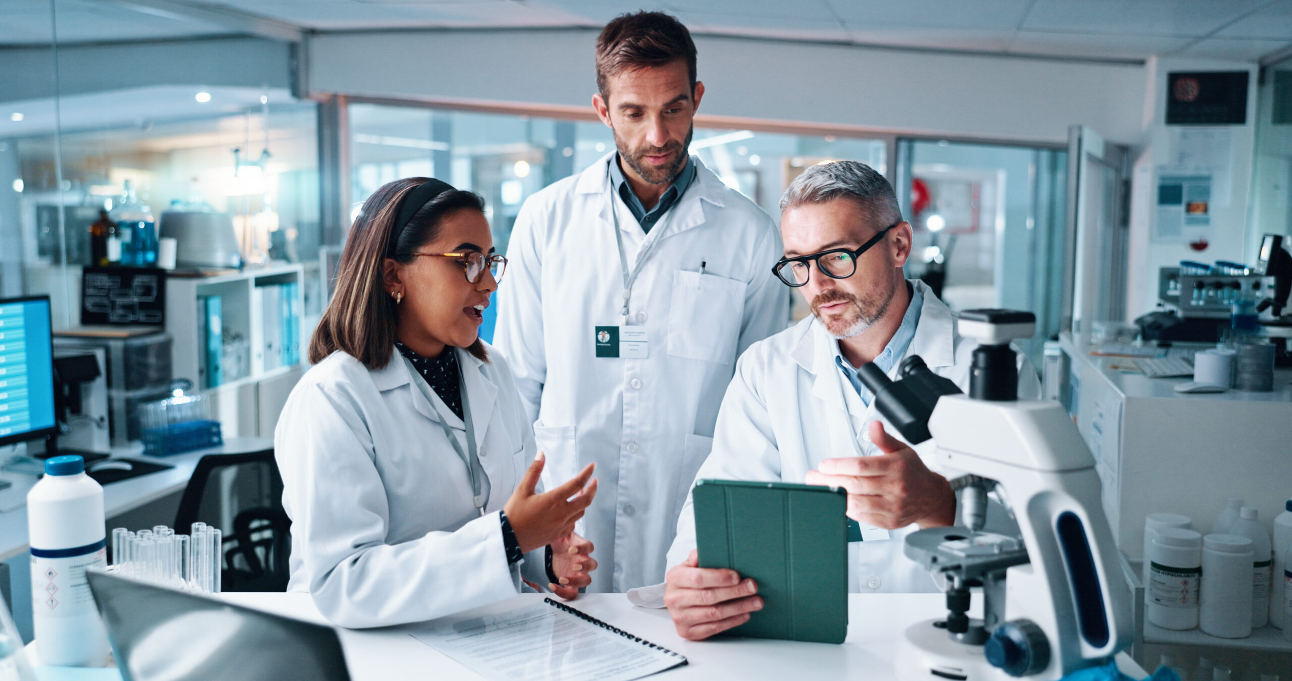 Discussion, science and tablet with people in laboratory together for breakthrough or development. Conversation, laptop and microscope with professional research team in clinical trial for discovery